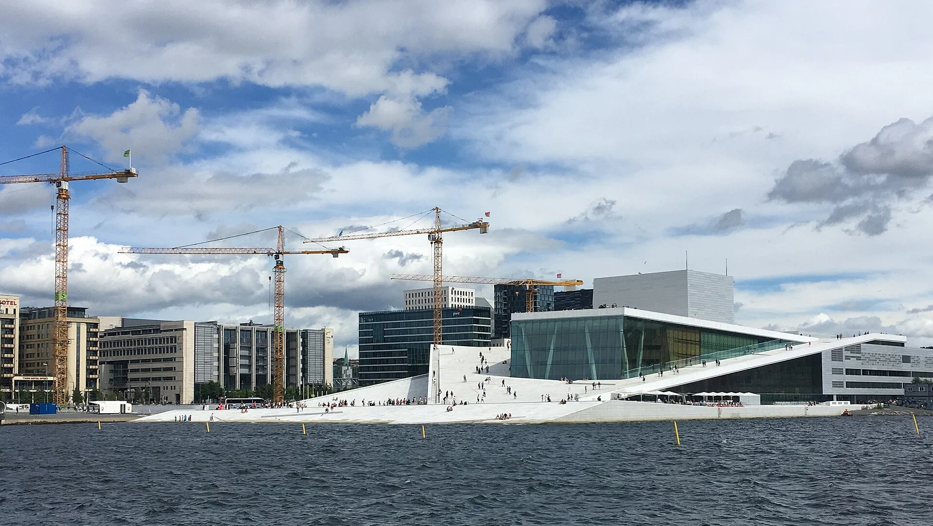 Das Opernhaus Oslo am Bjørvika, vom Wasser aus gesehen, mit Neubauten und Baukränen im Hintergrund.