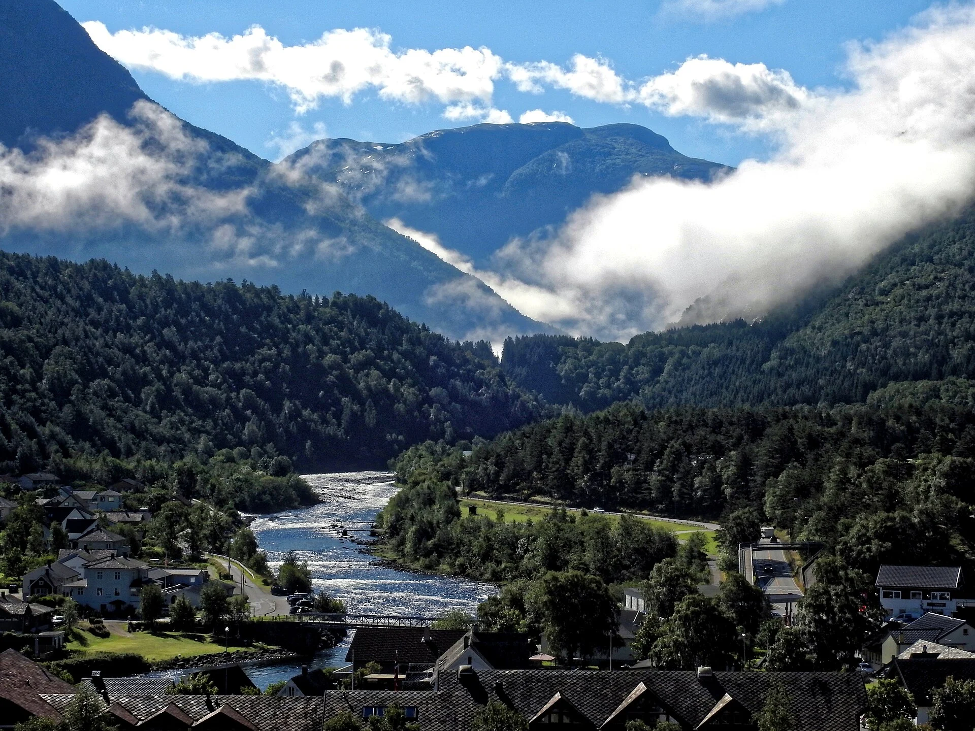 Blick über den Ortskern von Eidfjord mit dem Fluss Eio und bewaldeten Berghängen im Hintergrund.
